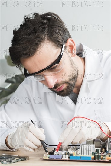 Technician examining computer motherboard with digital multimeter