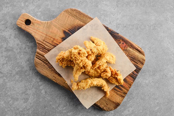 Top view of deep fried chicken nuggets in breading on wooden serving board