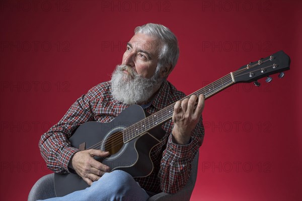 Contemplated senior man playing guitar against red background