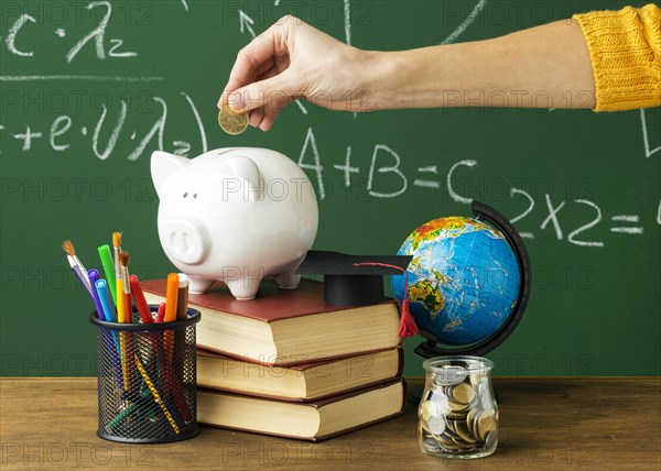 Person putting coins piggy bank with books pencils