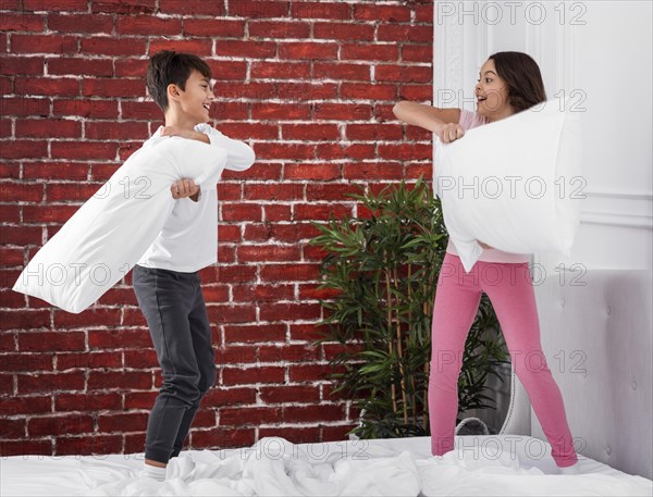 Young siblings home fighting with pillows