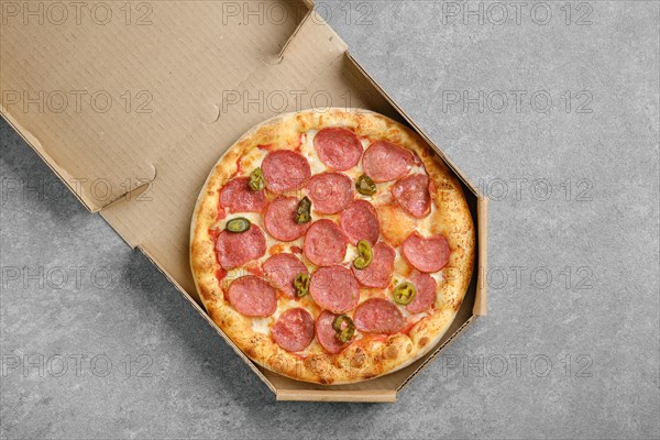 Top view of spicy pizza with sausage and pickled jalapeno pepper in cardboard box