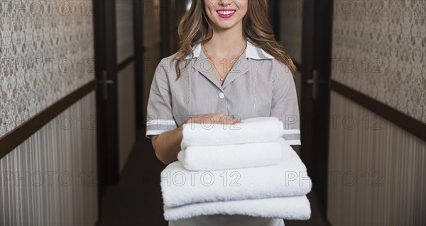 Portrait happy young maid standing corridor holding folded soft towels