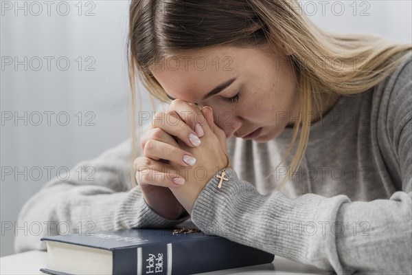 Young woman praying with holding cross necklace bible