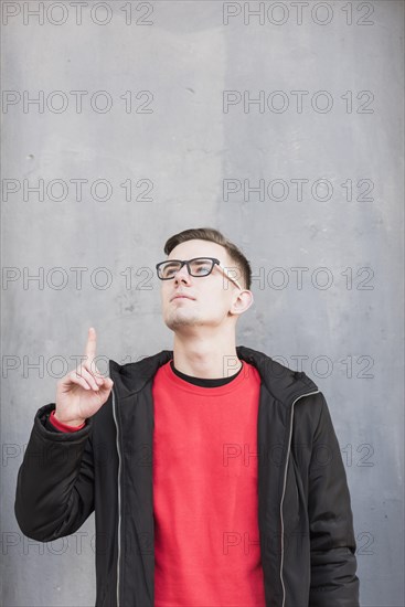 Handsome young man pointing his finger upward looking up against concrete wall