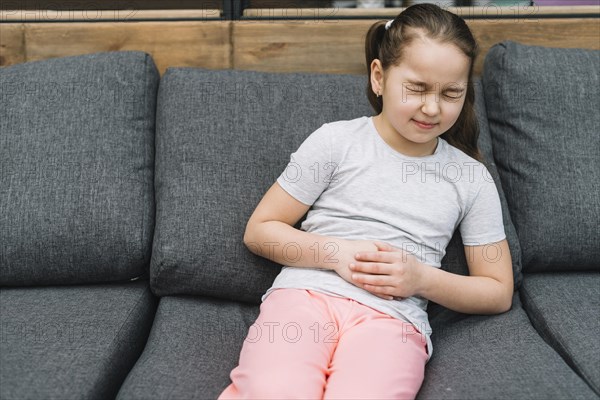 Portrait girl sitting gray sofa having sever pain stomach