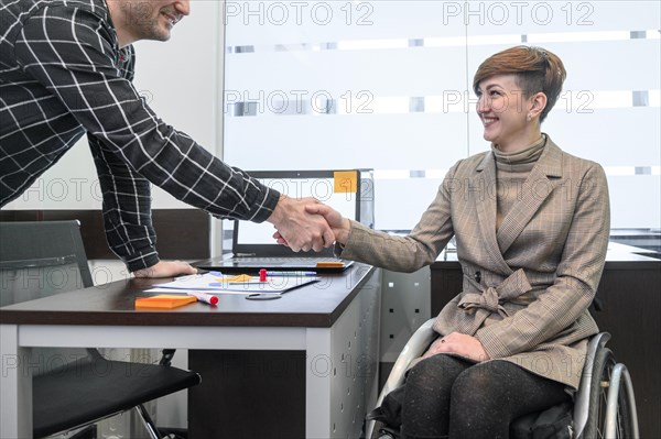 Confident businesswoman wheelchair shaking hands