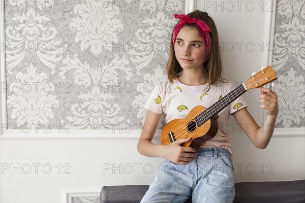 Smiling girl sitting sofa adjusting ukulele thinking