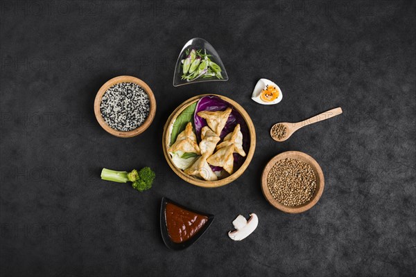 Top view dumplings steamers surrounded with sesame sauce coriander seeds broccoli mushroom black background