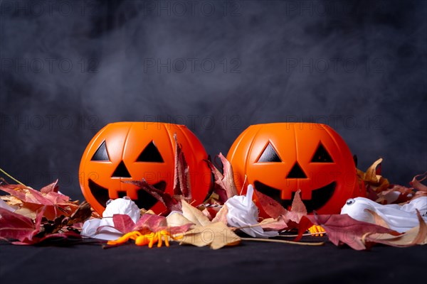 Halloween pumpkins over red autumn leaves and ghosts with smoke on a black background