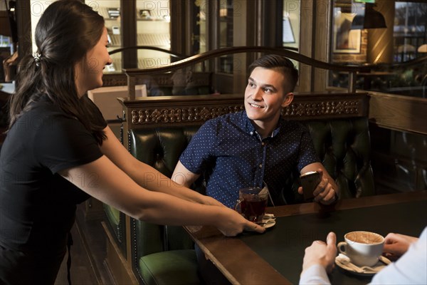 Cheerful waitress serving tea handsome man