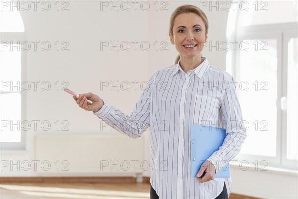 Front view smiley female realtor with clipboard empty house