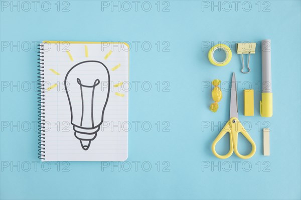 Overhead view hand drawn light bulb notebook with stationary blue background