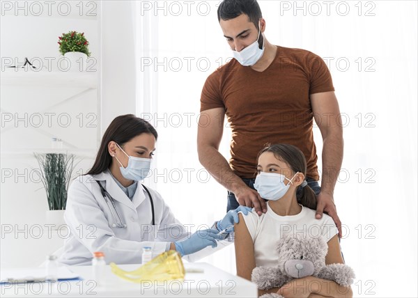 Girl holding her toy while being vaccinated