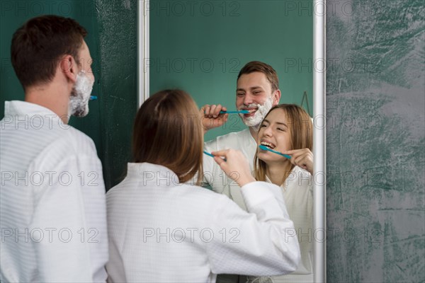 Couple wearing bathrobes brushing teeth mirror