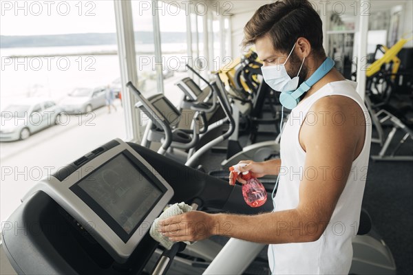 Side view man with medical mask disinfecting treadmill gym