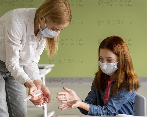 Teacher with medical mask disinfecting child s hands classroom