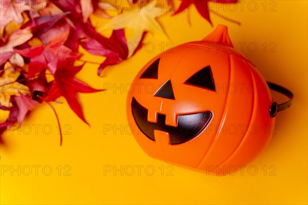 A Halloween pumpkin on red autumn leaves and a yellow background