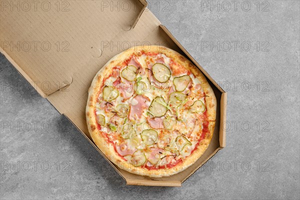 Top view of pizza with ham and pickled cucumber in takeaway cardboard box