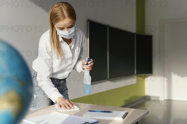 Female teacher disinfecting her desk classroom