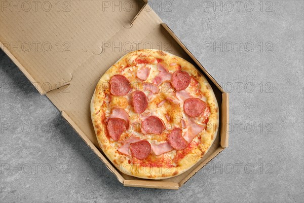 Top view of pizza with sausage and pork ham in cardboard box