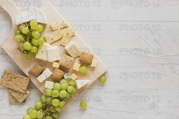 Overhead view cheese blocks crisp bread grapes wooden desk