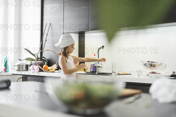 Girl with chef hat washing her hand faucet home