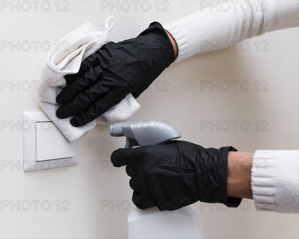 Hands with gloves disinfecting light switch