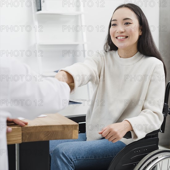 Smiling portrait disabled young woman sitting wheelchair shaking hands with person workplace