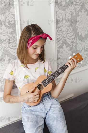 Smiling little girl playing ukulele home