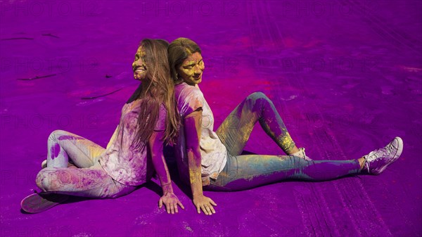 Smiling young women sitting back back sitting holi color powder