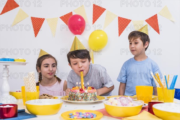 Two friends looking boy blowing out candles birthday cake