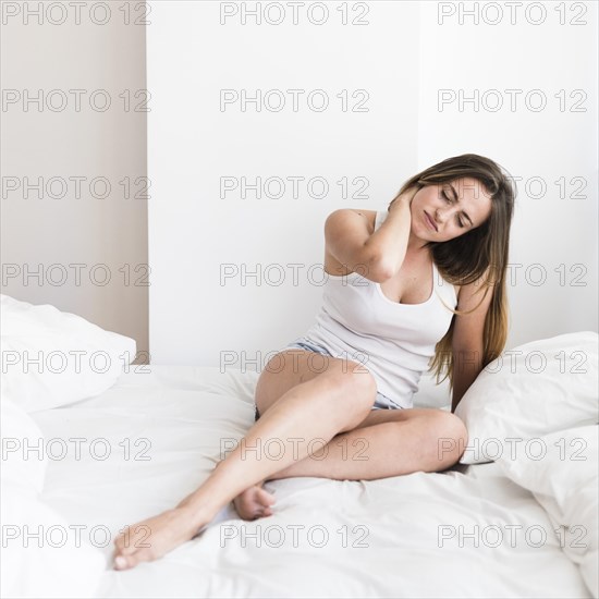 Young woman sitting bed suffering from neck pain