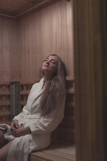 Woman white bathrobe sitting wooden bench relaxing sauna