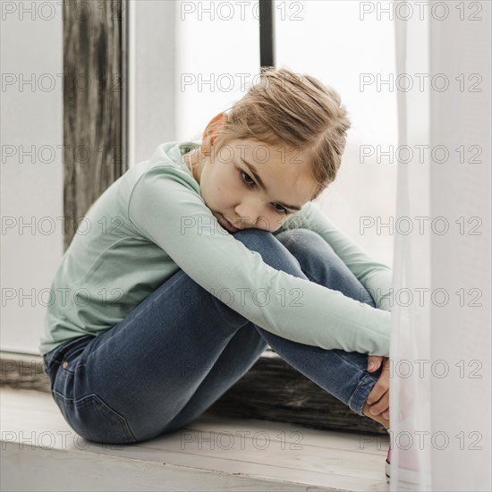 Bored little girl sitting window sill