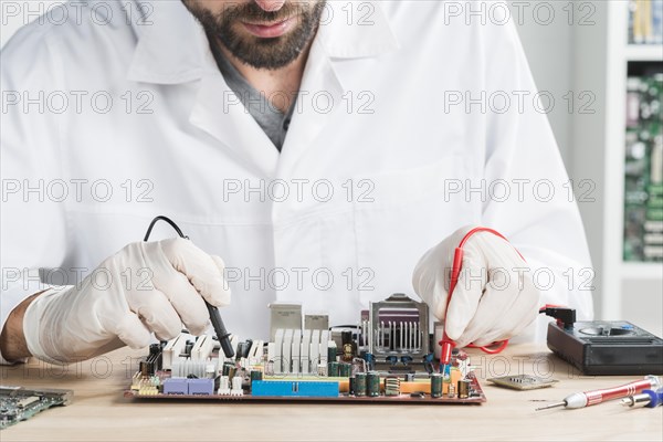 Male technician checking computer with digital multimeter wooden desk