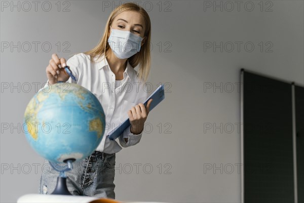 Female teacher classroom with clipboard pointing globe