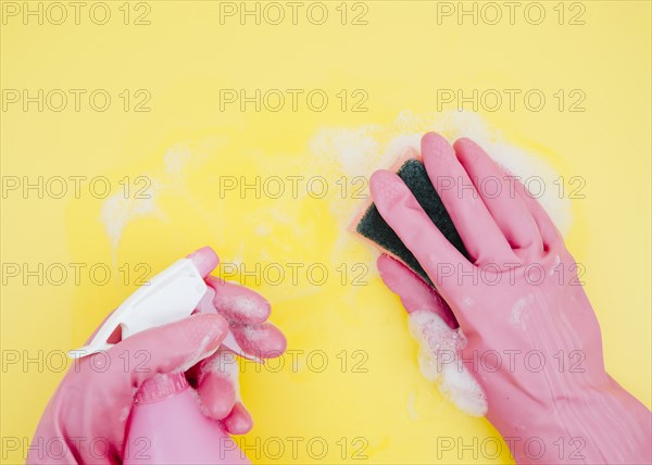 Close up cleaner cleaning yellow backdrop with sponge spray bottle