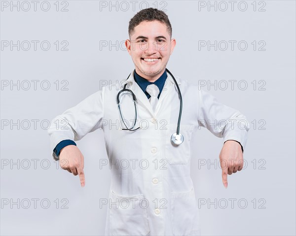 Young doctor pointing a promotion down. Happy doctor pointing fingers down. Latin doctor pointing down an isolated advertising space