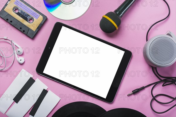 Cassette tape cd earphone vinyl record microphone speaker paper piano keys around digital tablet pink background