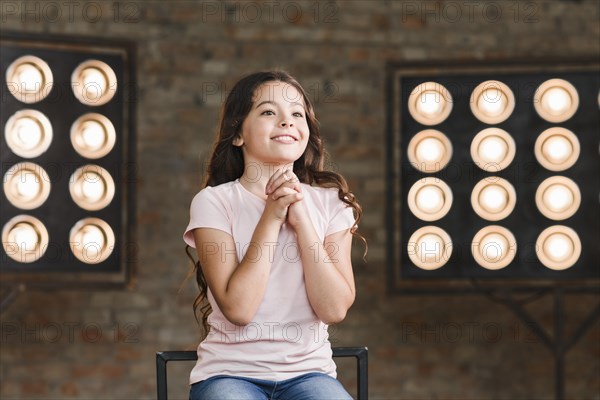 Smiling girl sitting against stage light clapping her hands