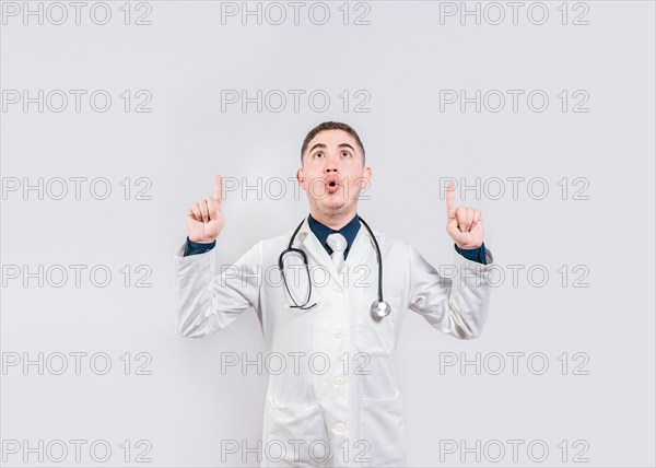 Surprised doctor pointing an advertisement up. Amazed doctor pointing a promotion up. Male doctor looking and pointing up isolated