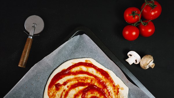 Pizza dough with sauce near vegetables