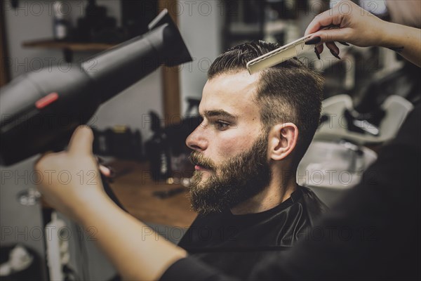 Crop woman drying hair man barbershop