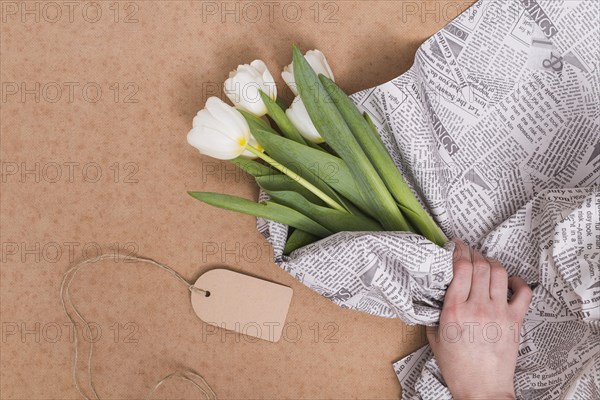 Person s hand wrapping white tulip flowers newspaper with price tag brown background