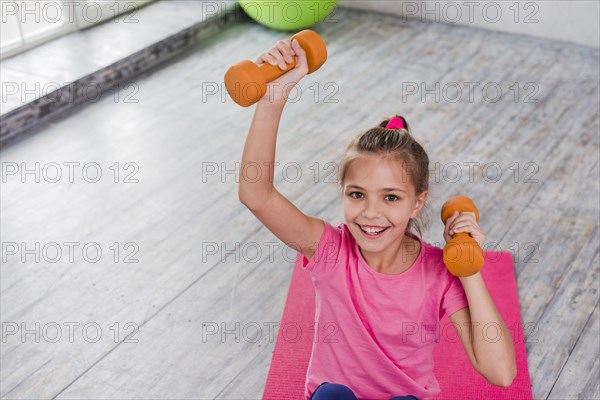 Portrait smiling girl exercising with orange dumbbell