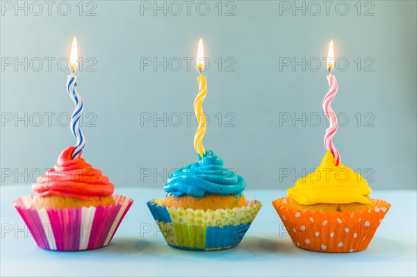 Row cupcakes with burning candles blue backdrop