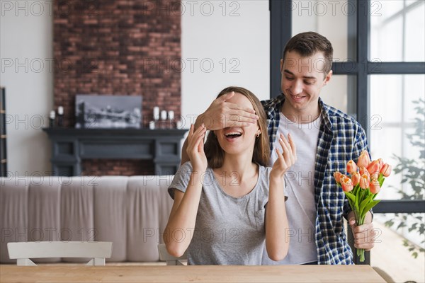 Man with flowers surprising cheerful woman
