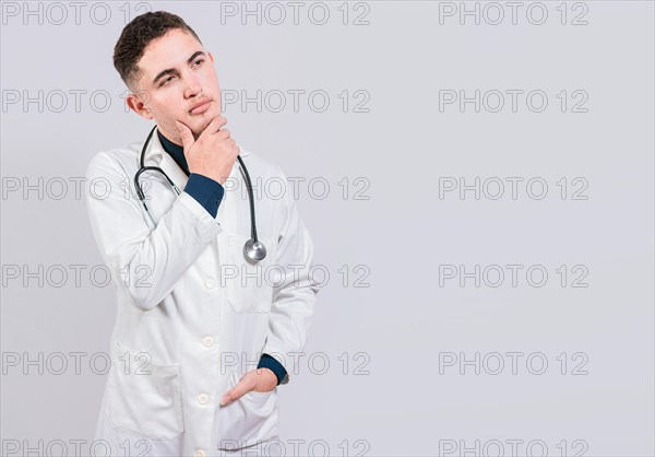 Doctor thinking with hand on chin. Pensive doctor man looking up