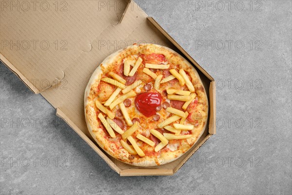 Top view of pizza with various sausages and french fries in cardboard box
